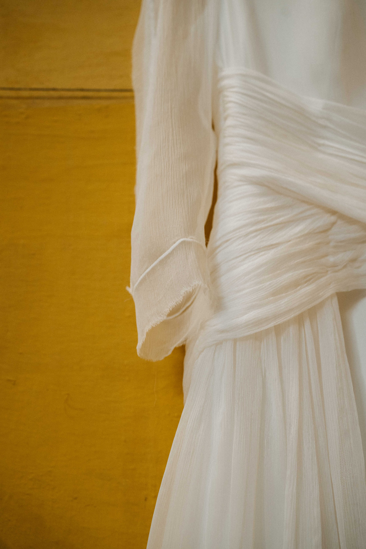 Vestido de novia plisado en color marfil, colgado junto a una pared ocre
