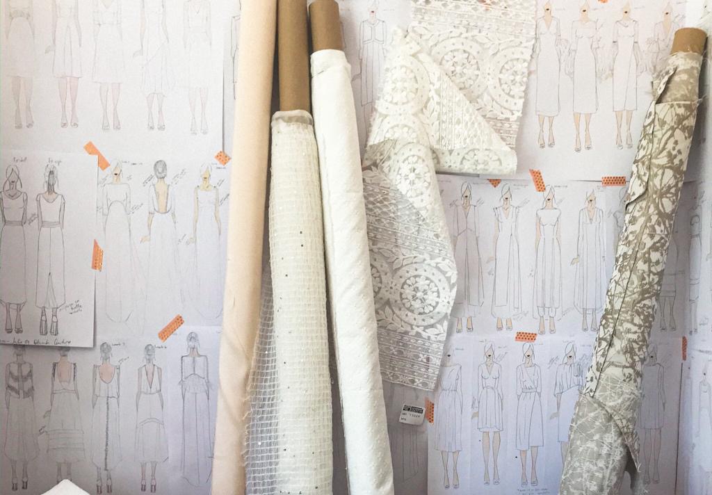 Rollos de tejido y bocetos de vestidos en la mesa de trabajo del taller